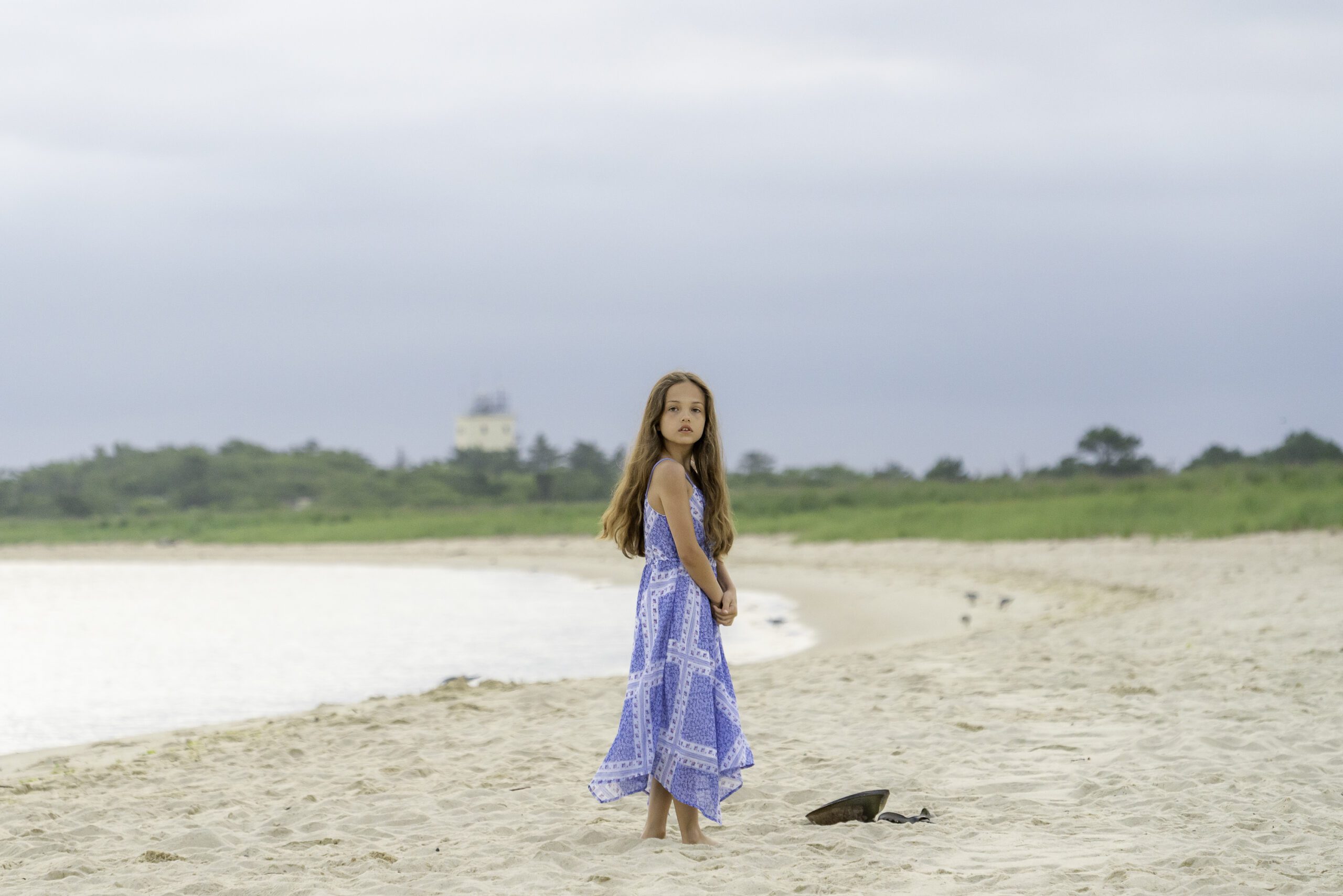 a young girl standing on the beach next to a bird
