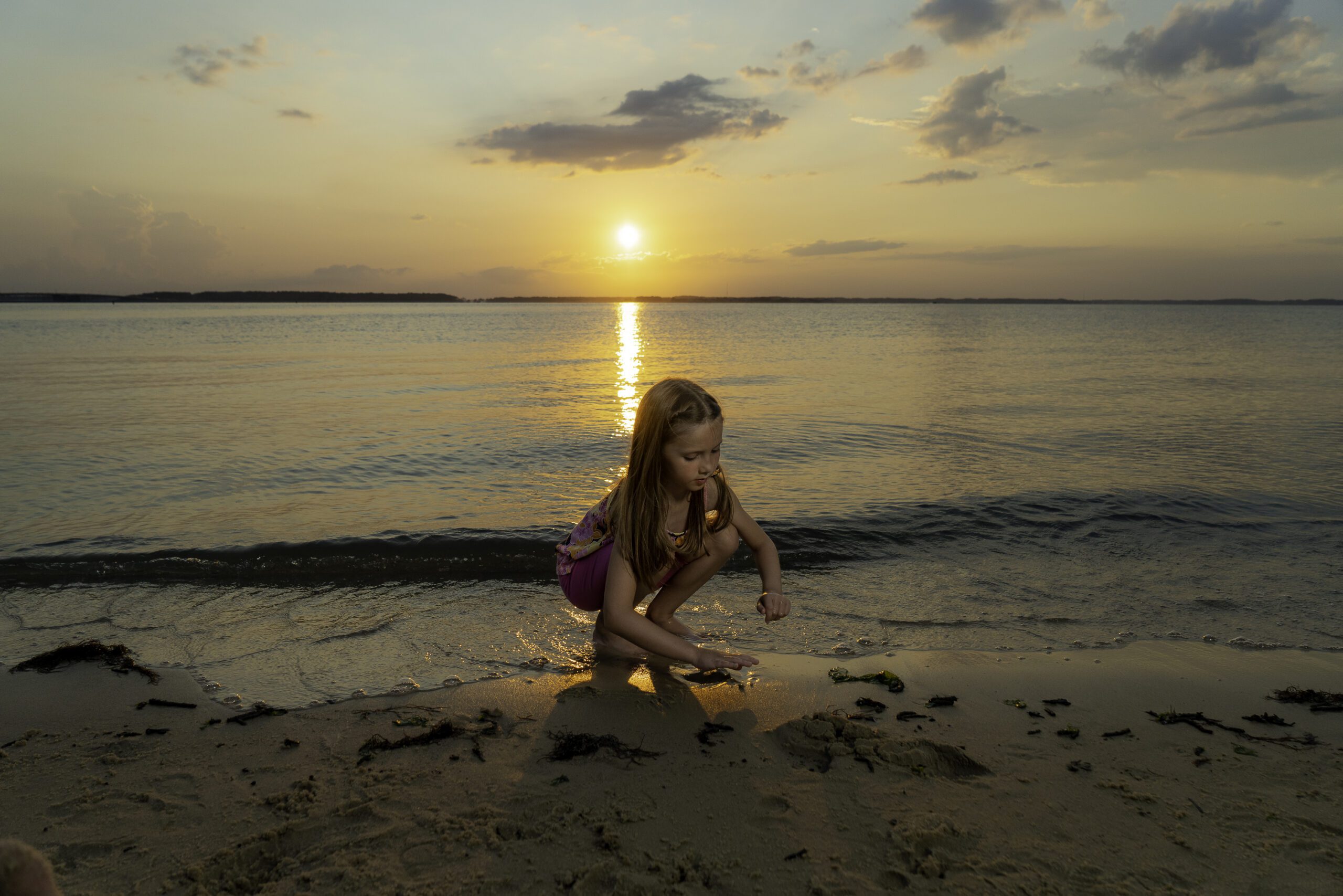 a little girl sitting on the beach at sunset