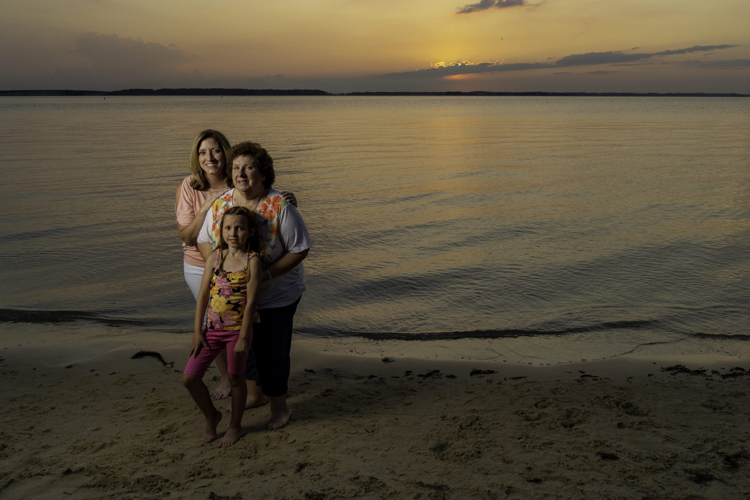 three women and a child standing on the beach at sunset