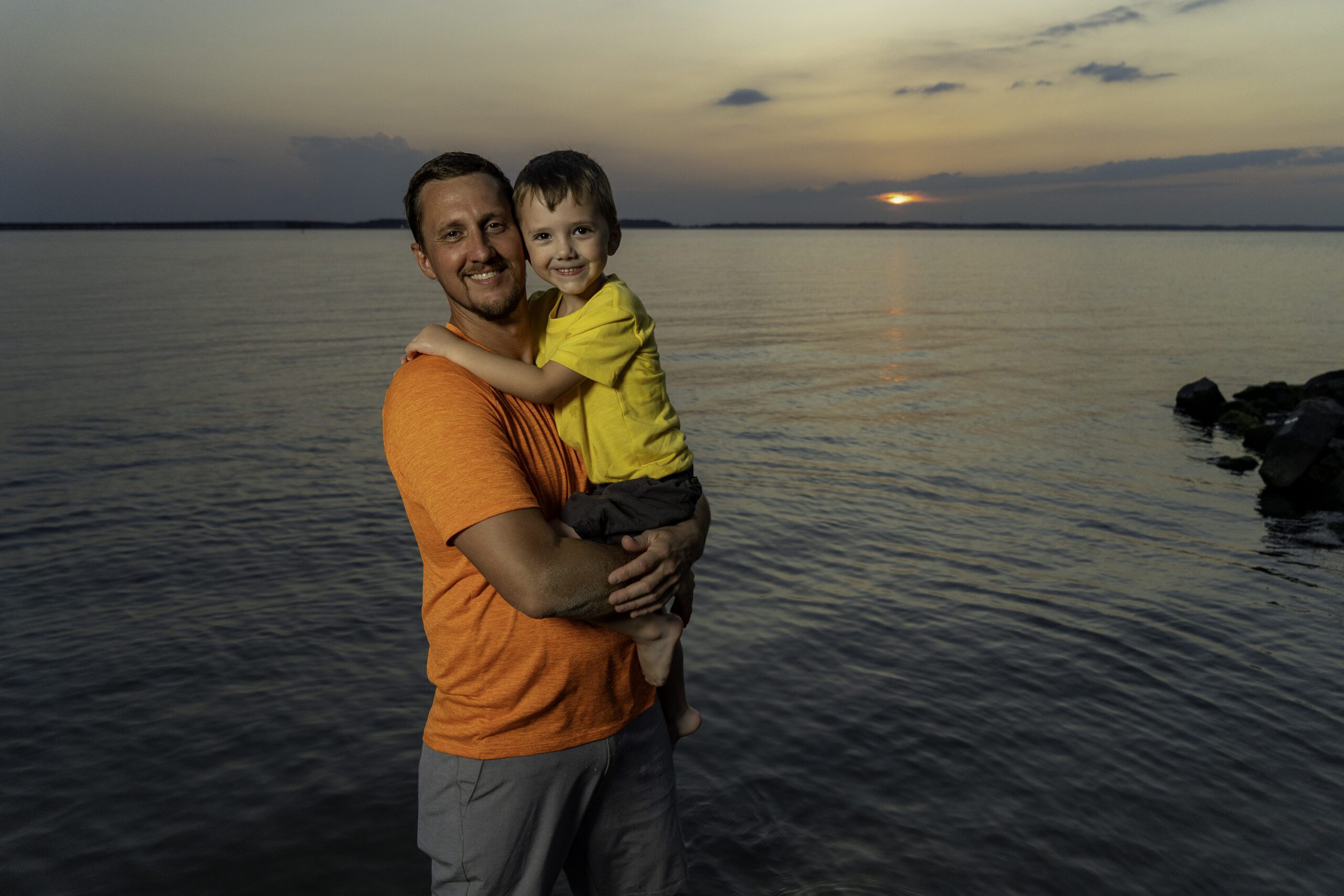 a man holding a child in his arms near the water
