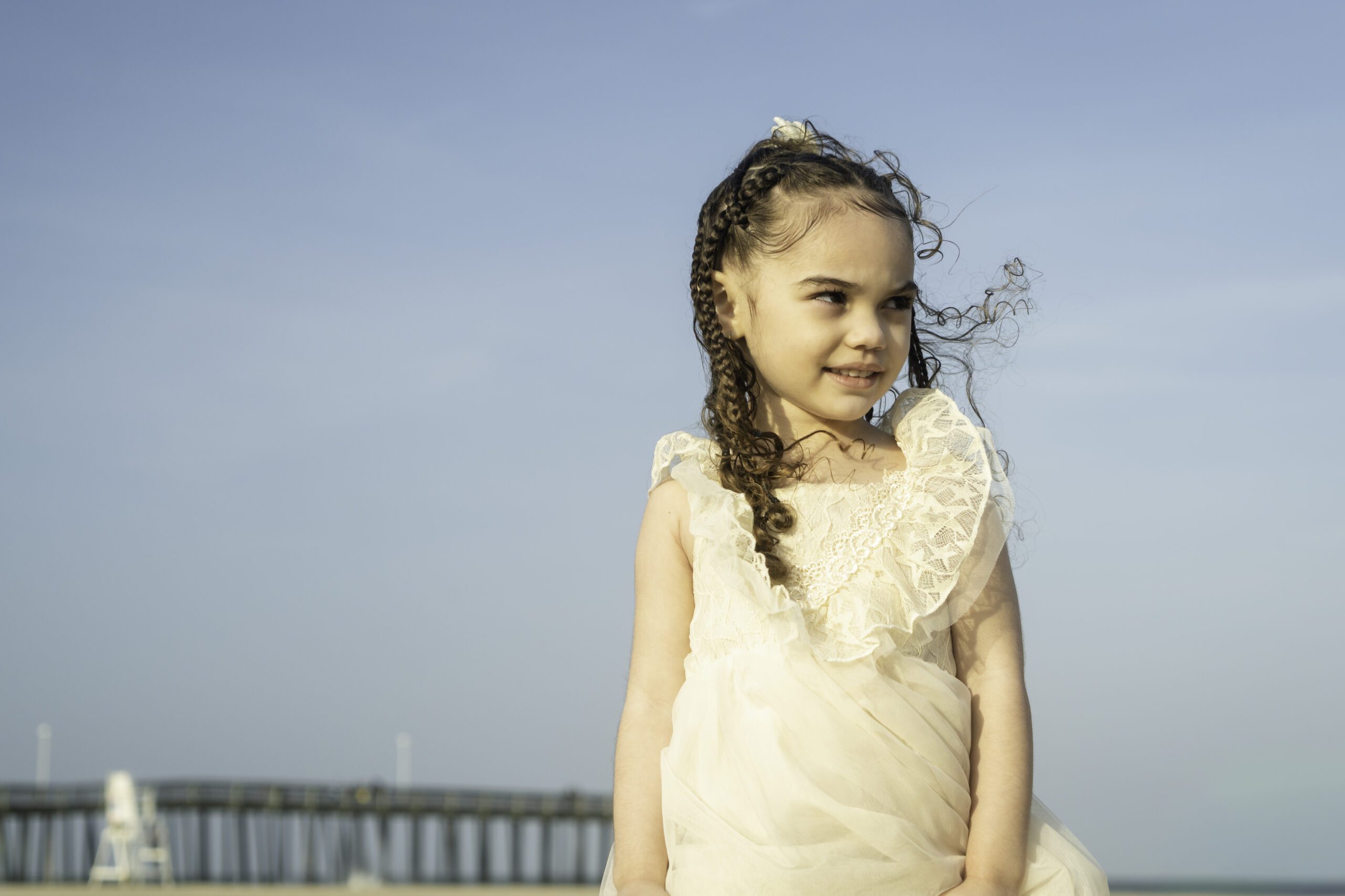 a little girl in a white dress standing on the beach