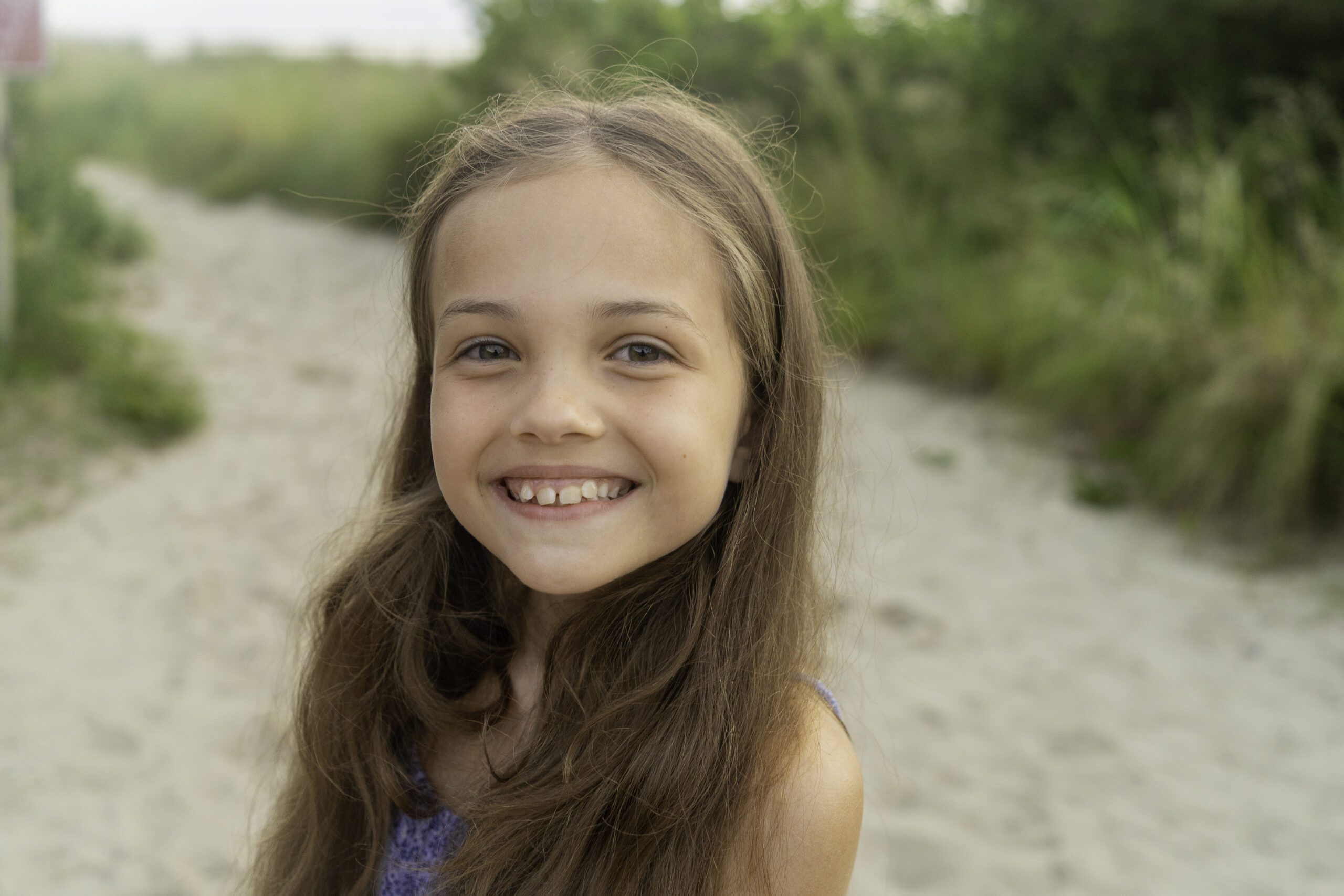 a young girl smiling at the camera on a beach