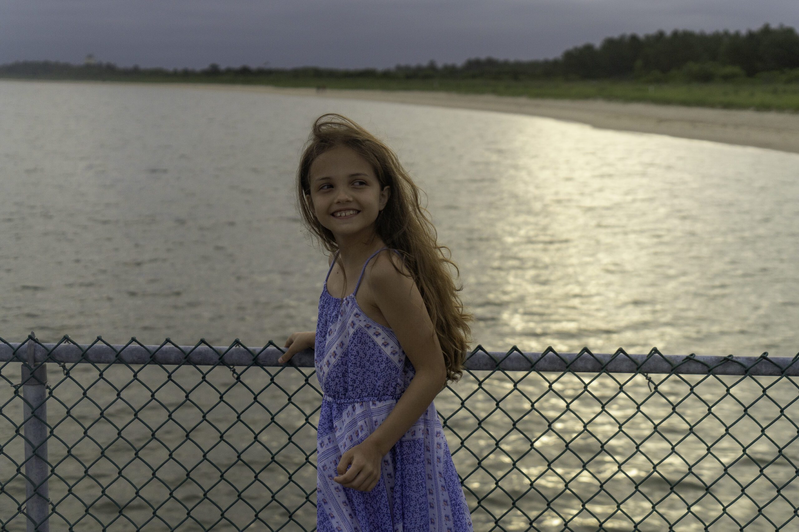 a young girl standing next to a fence near the water