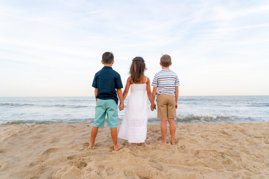 three children standing on the beach holding hands