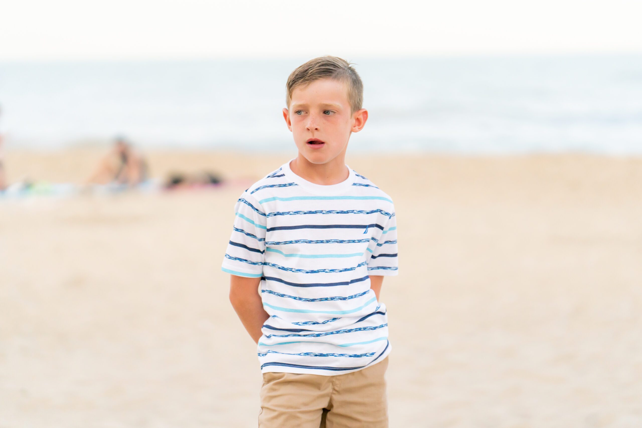 a young boy standing on the beach with his hands in his pockets
