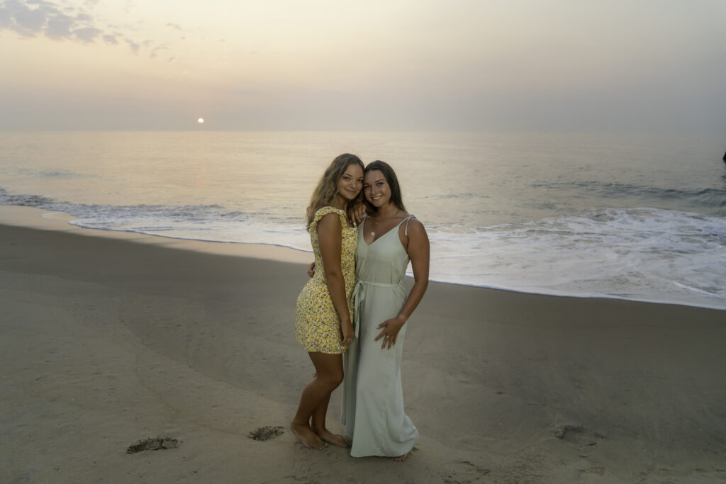two women standing on the beach next to the ocean