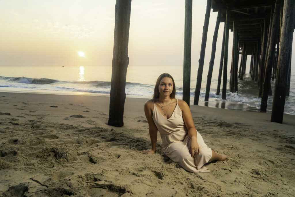 a woman sitting on the beach in front of a pier