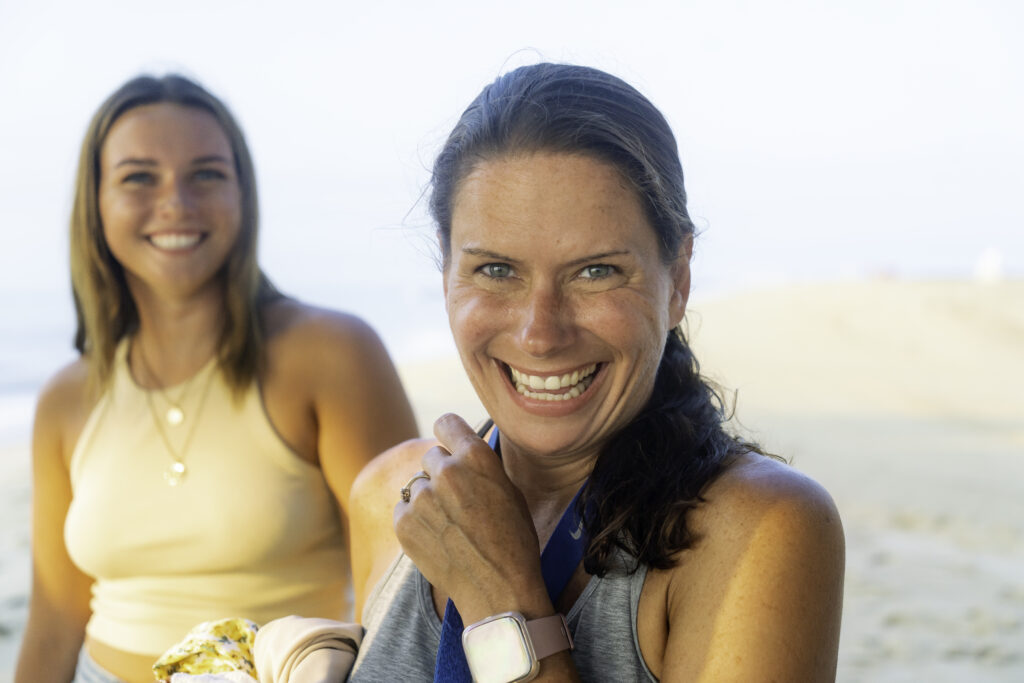 two women sitting on the beach smiling for the camera