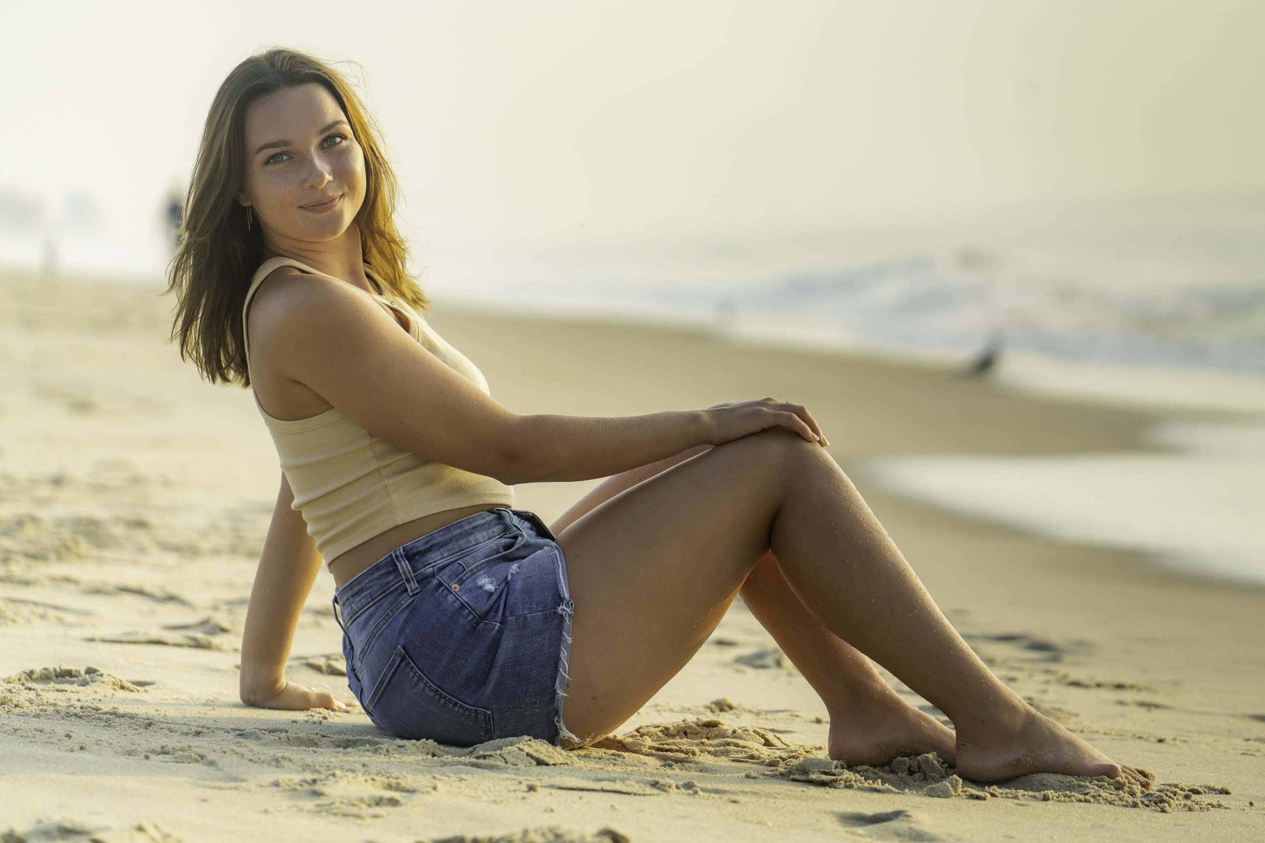 a woman sitting on the beach with her legs crossed