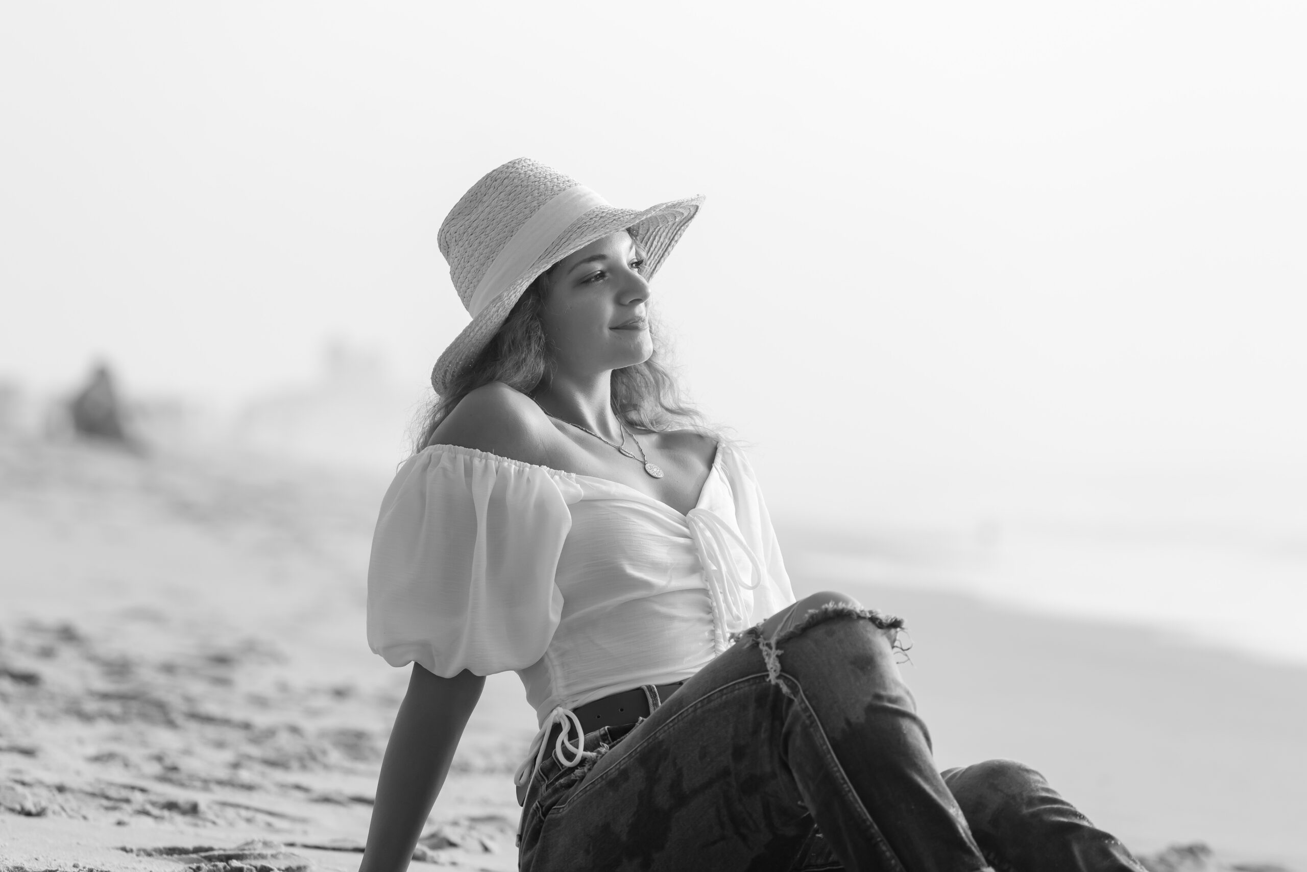 a woman sitting on the beach wearing a hat