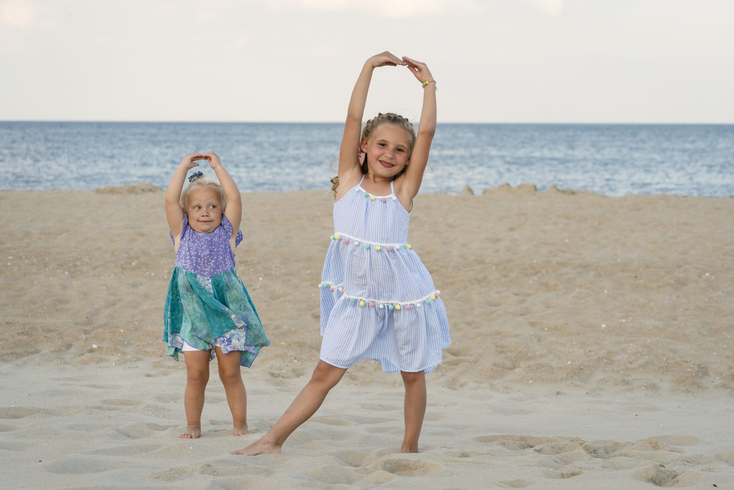 two little girls standing in the sand with their hands up