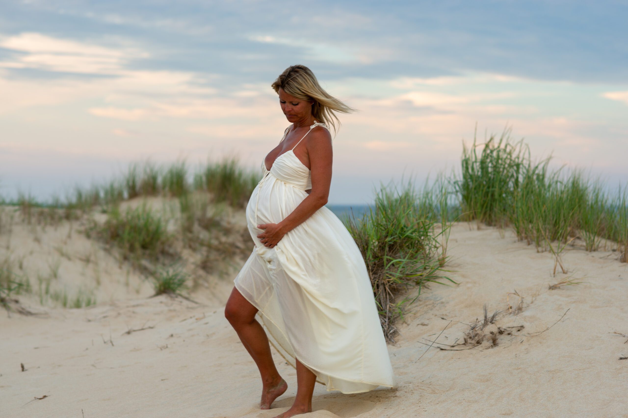 a pregnant woman in a white dress walking on the beach