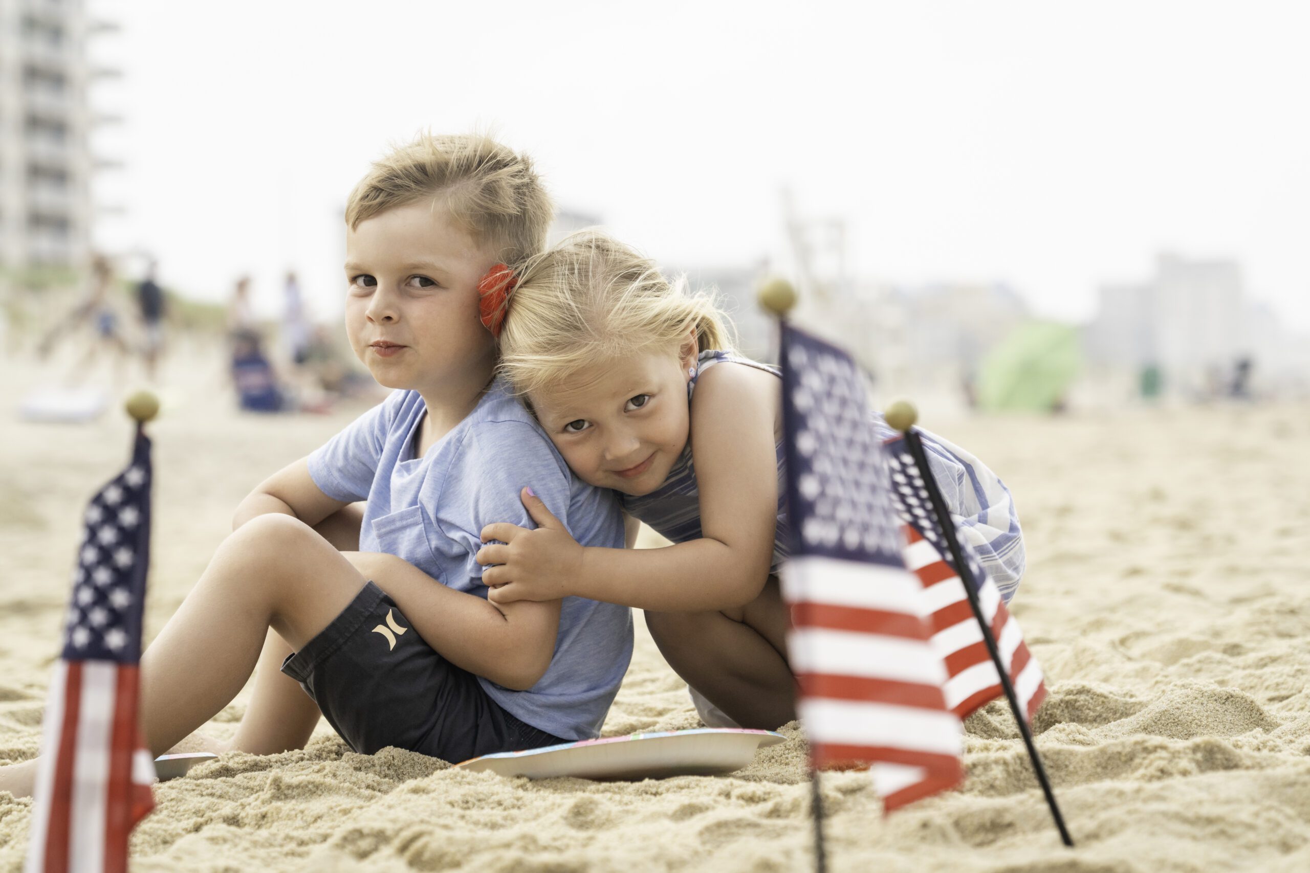 two young girls hugging on the beach with american flags