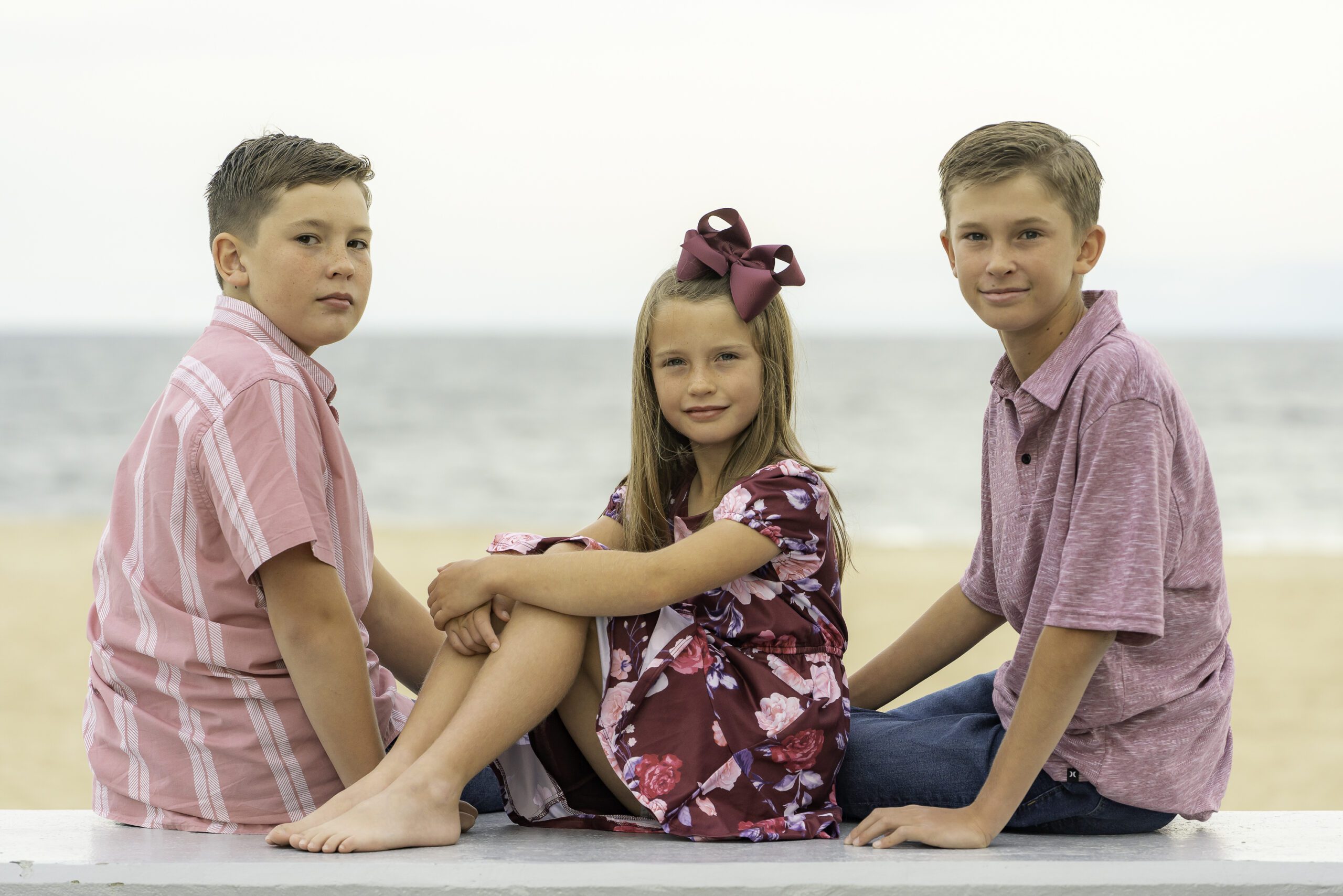 three young children sitting on the beach posing for a photo