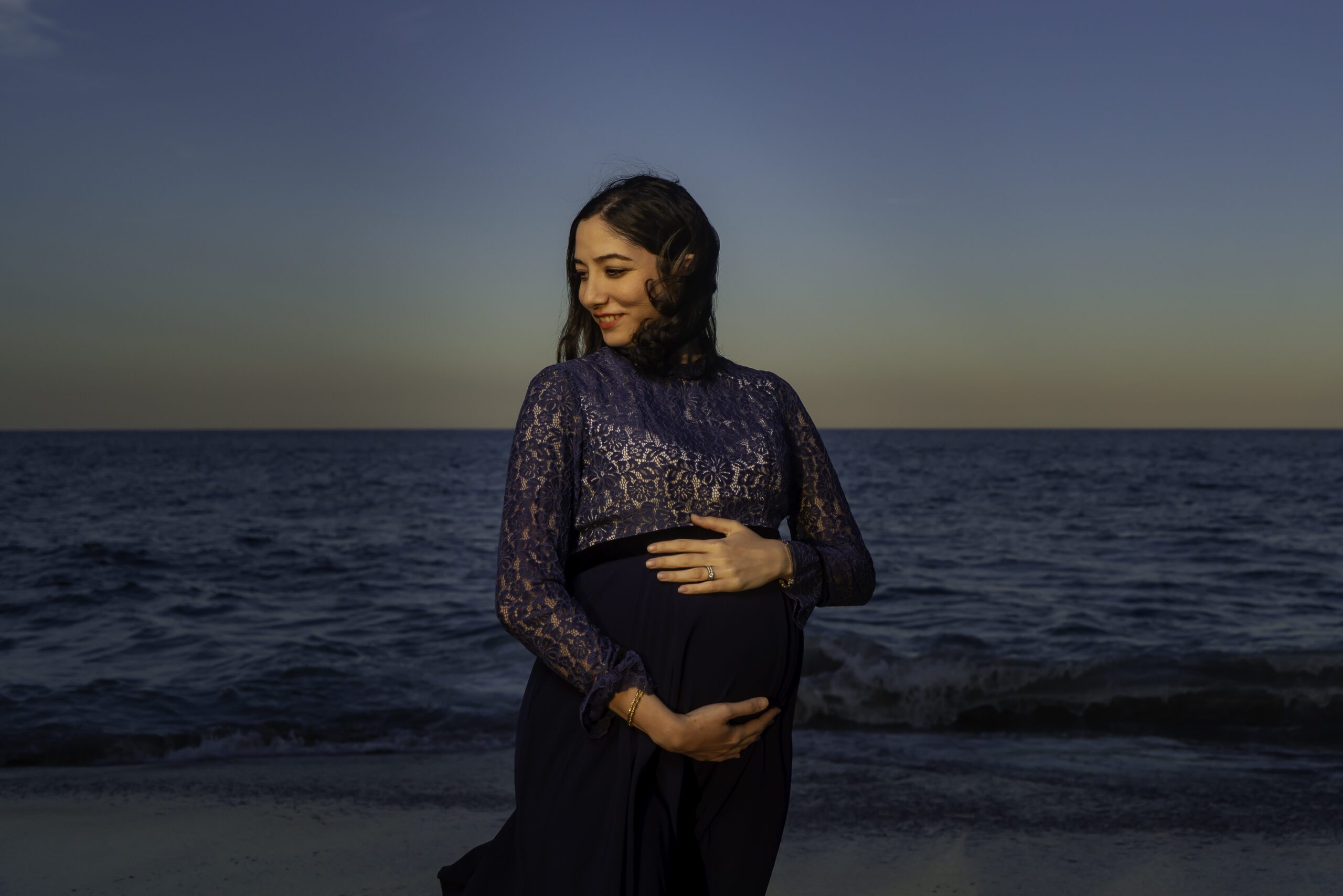 a pregnant woman standing on the beach at sunset
