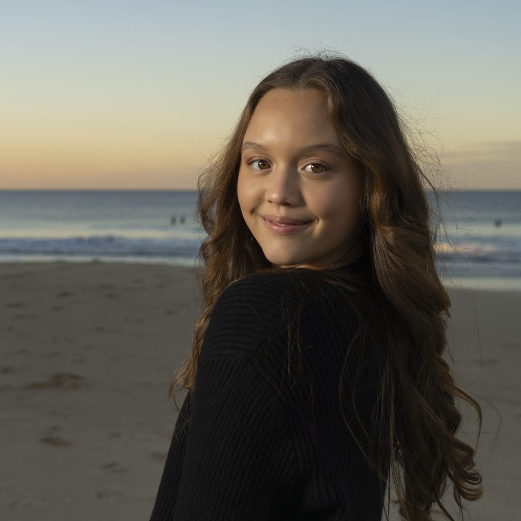 a young girl standing on the beach at sunset