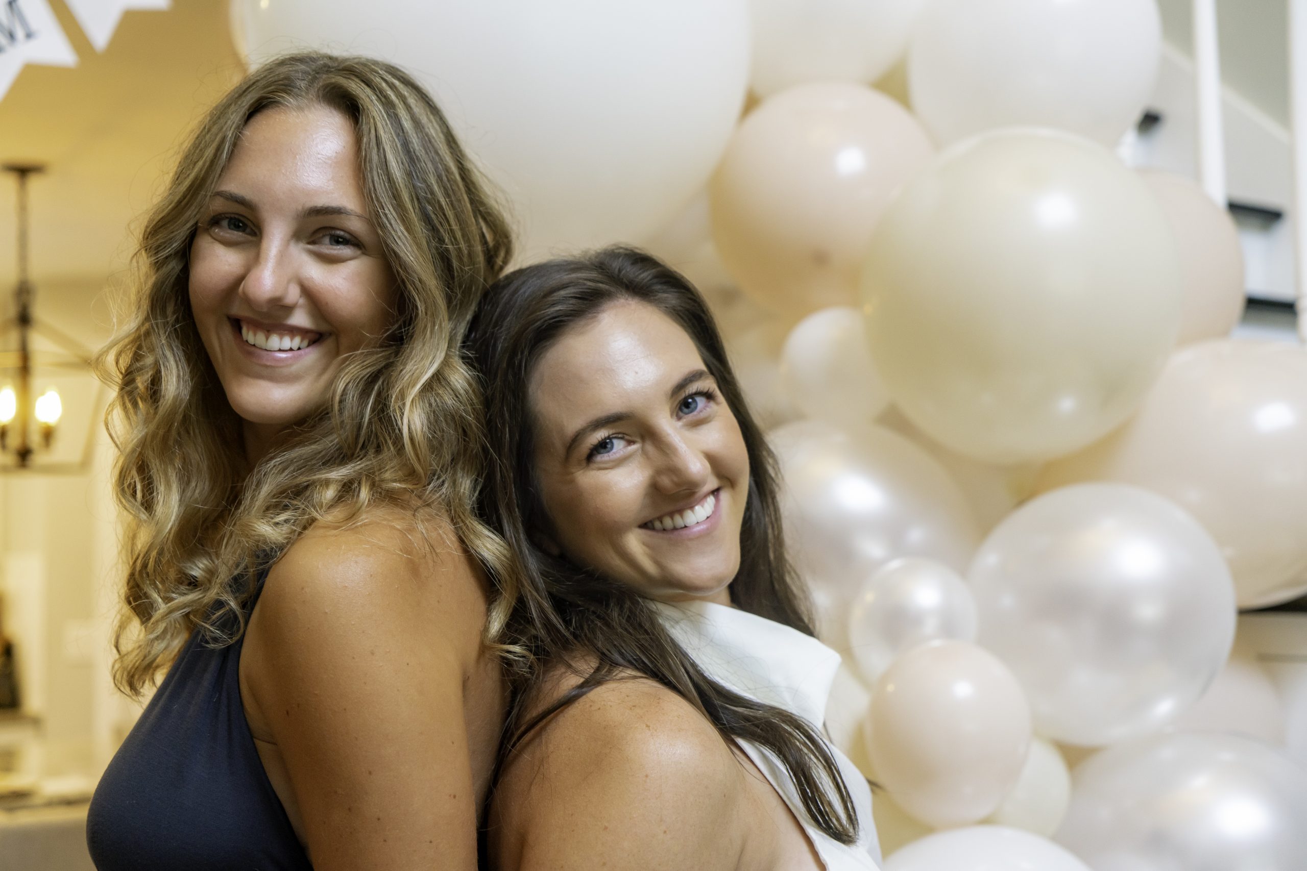 two women standing next to each other in front of balloons