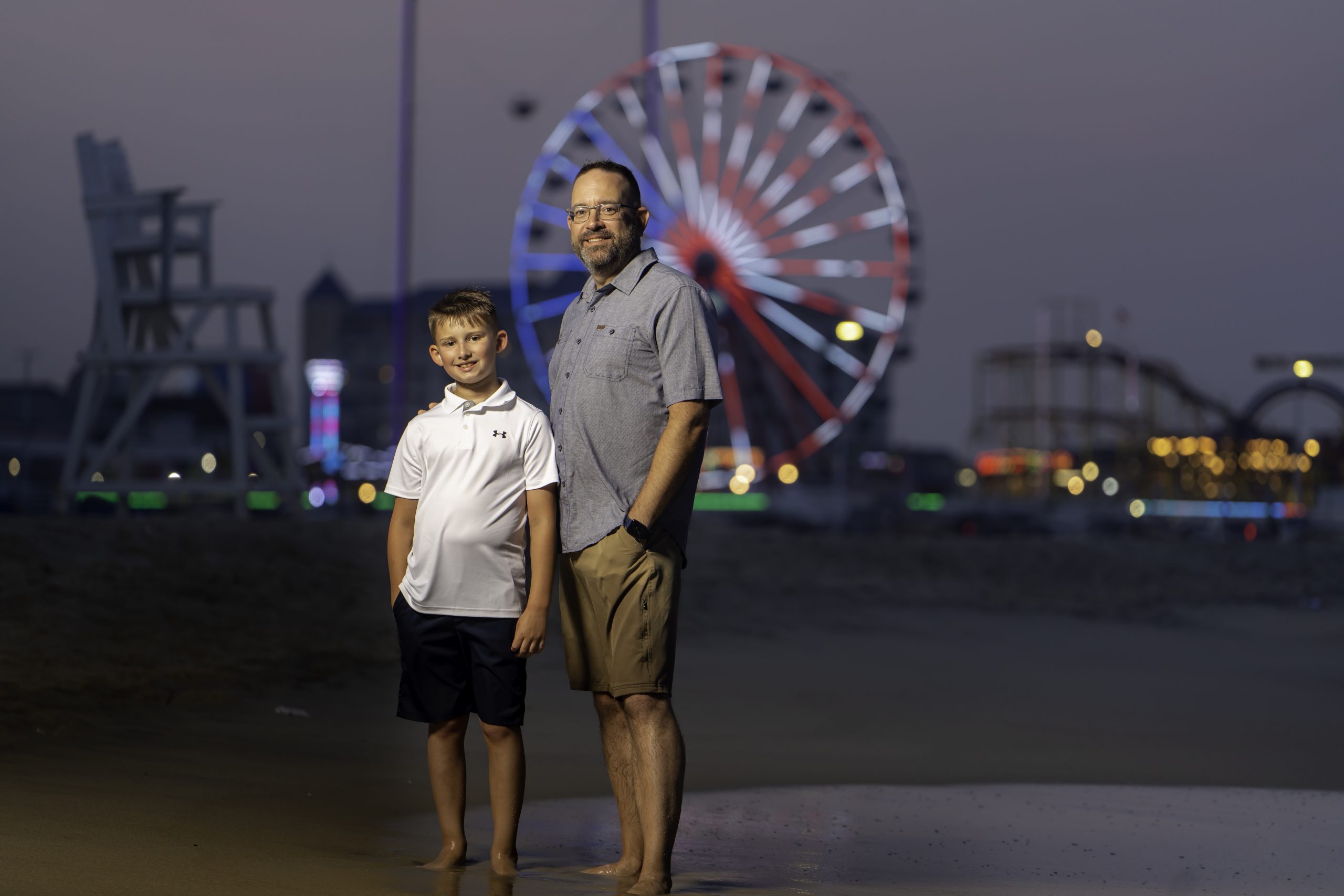a man and boy standing on the beach in front of a ferris wheel