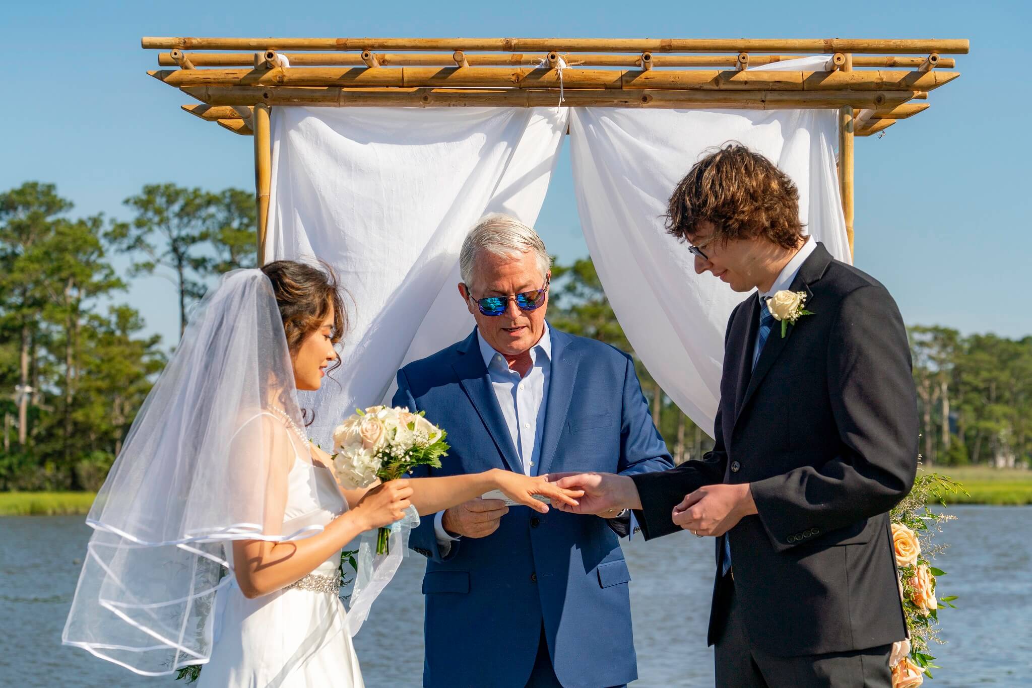 Bride and groom exchanging rings at the alter by the water