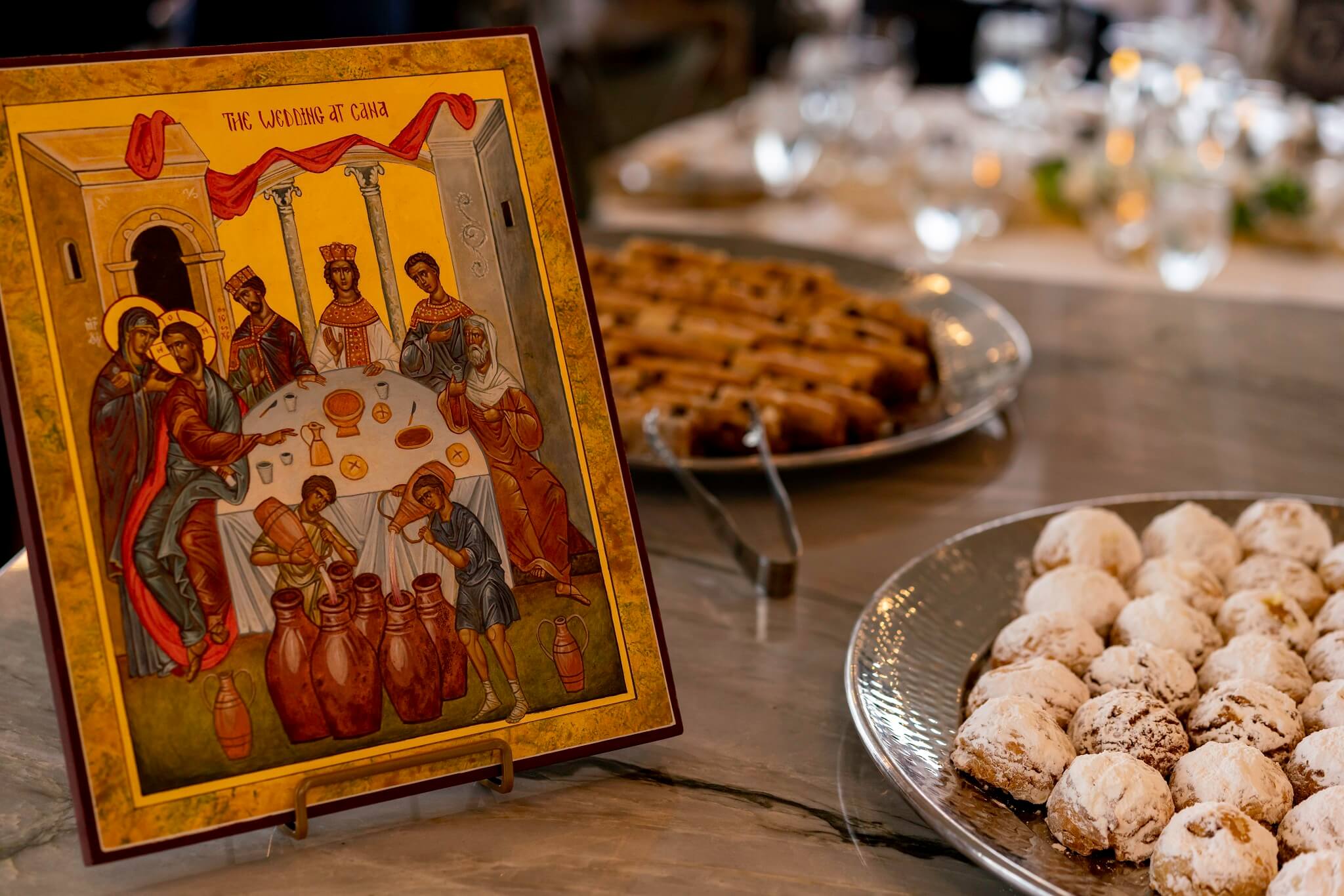 Framed artwork of the Wedding at Cana beside different pastries