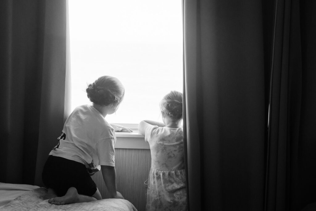 two little girls looking out the window at the ocean