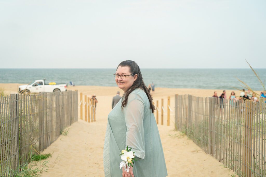 a woman in a green dress walking down a path to the beach