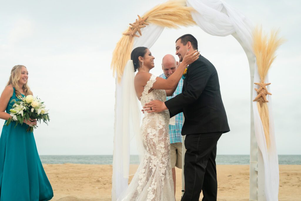 a bride and groom are standing under an arch on the beach