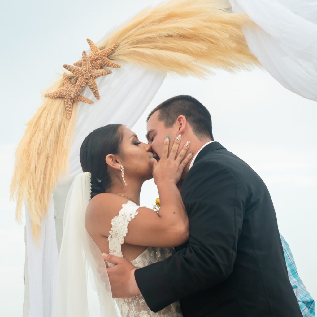 a bride and groom kissing under a starfish arch