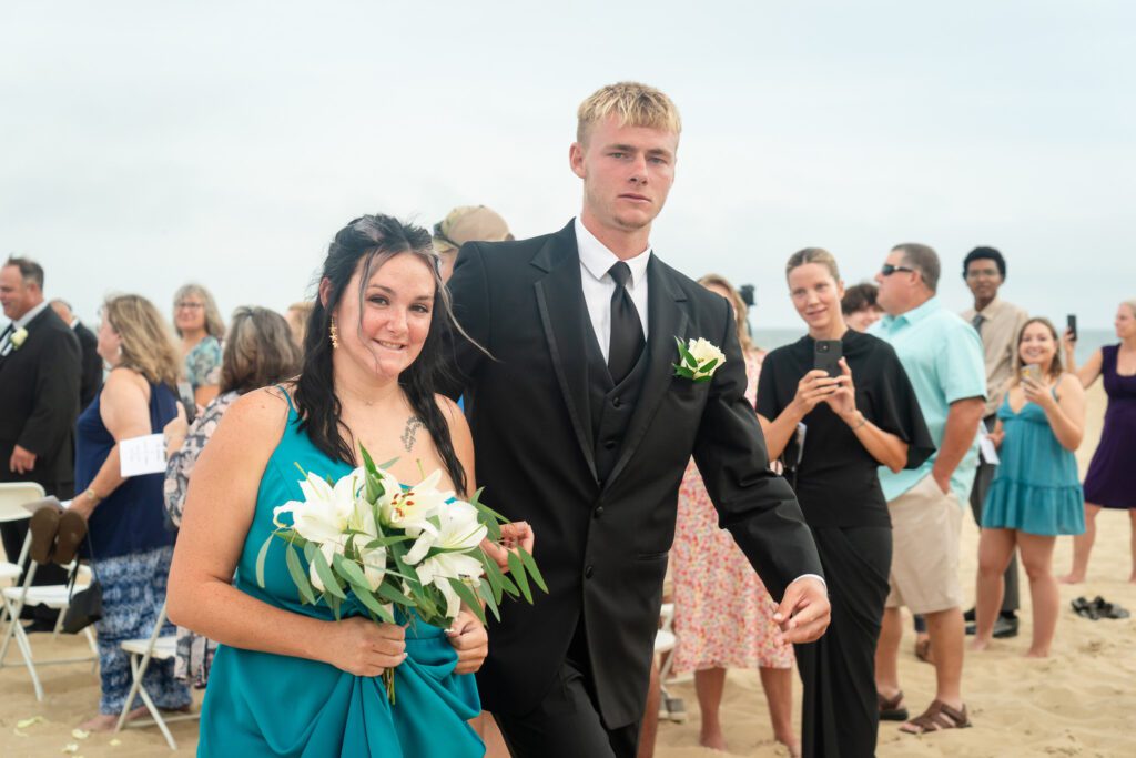 a man and woman in formal wear walking on the beach