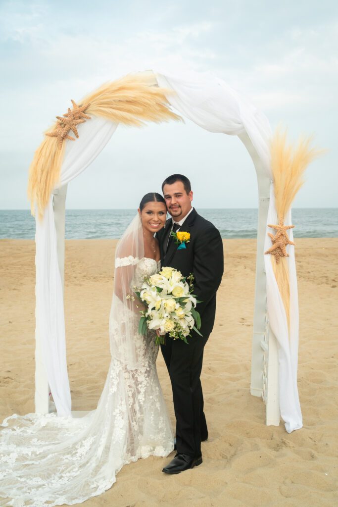 a bride and groom pose for a photo on the beach