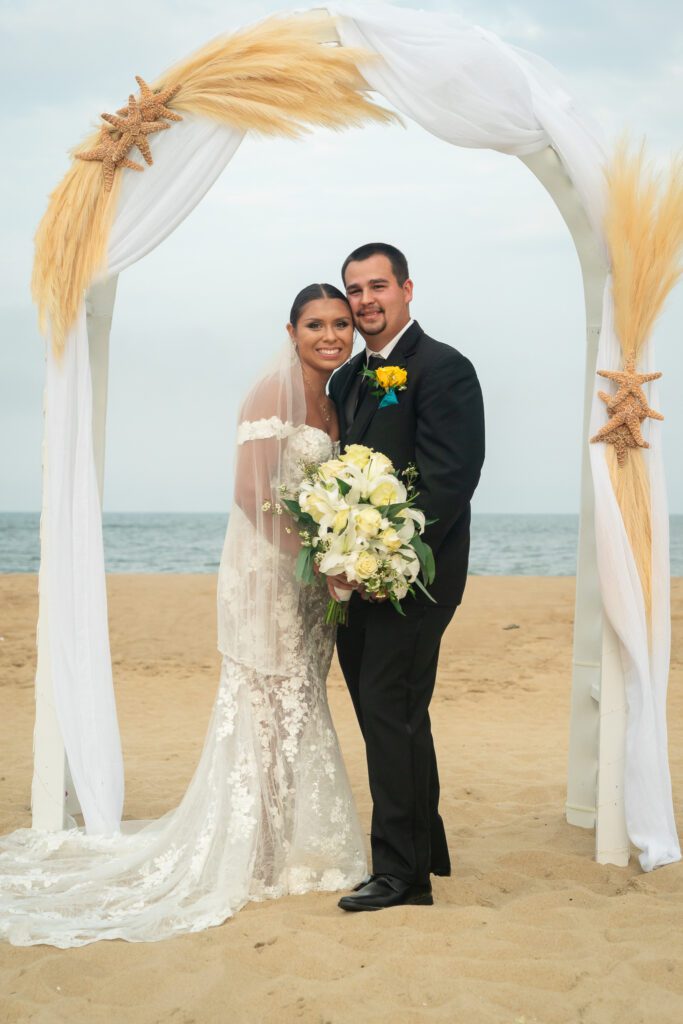 a bride and groom pose for a photo on the beach