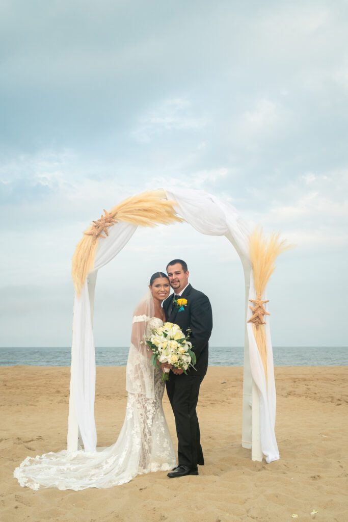 a bride and groom standing under an arch on the beach
