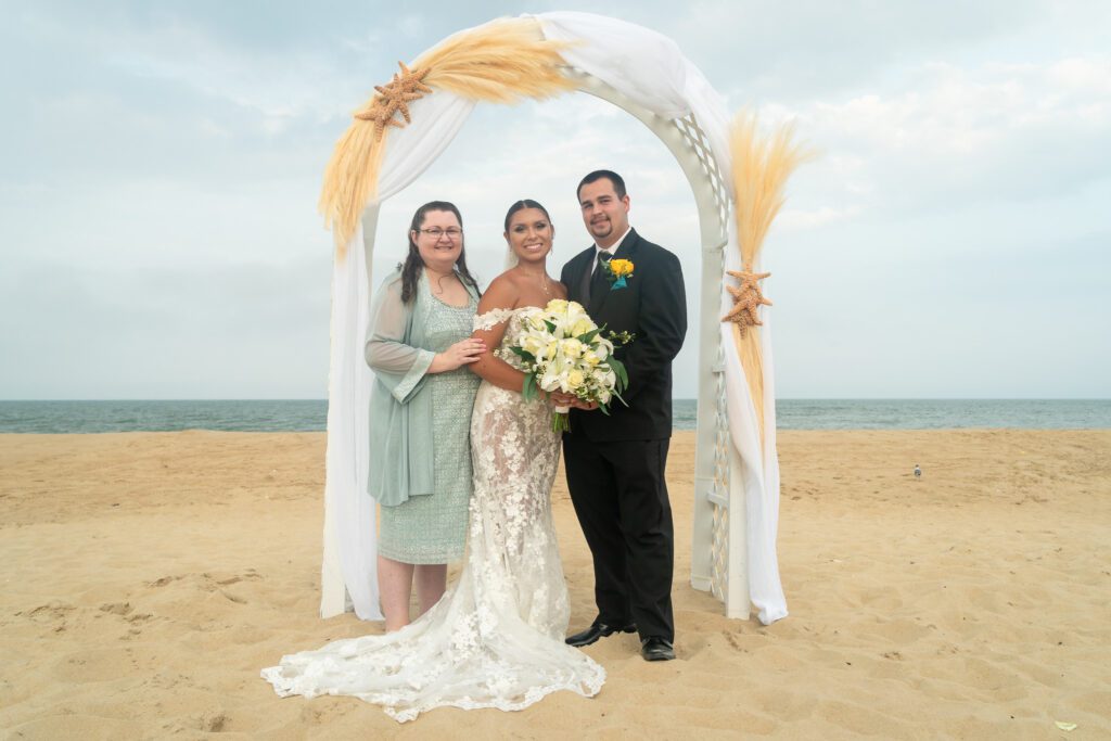 a man and two women standing under an arch on the beach
