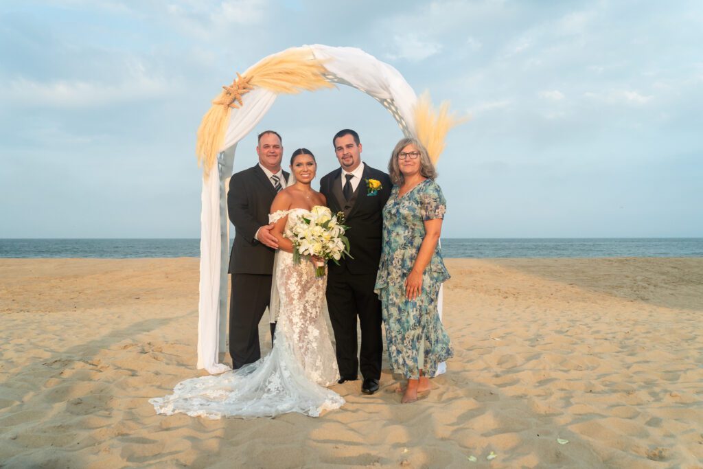 a bride and groom with their parents on the beach