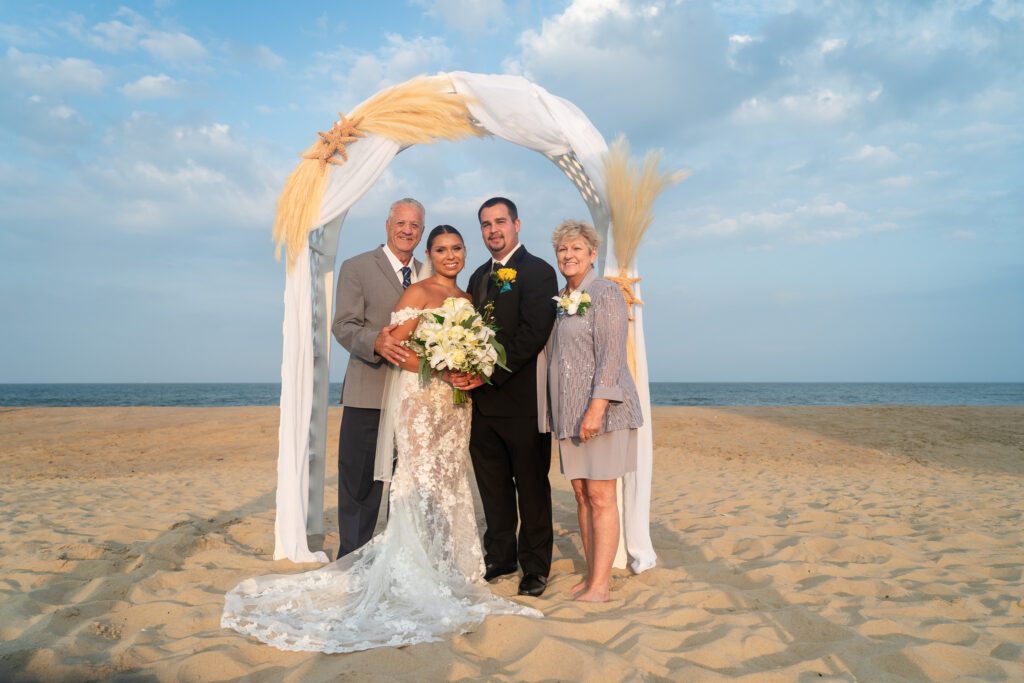 a bride and groom with their parents on the beach