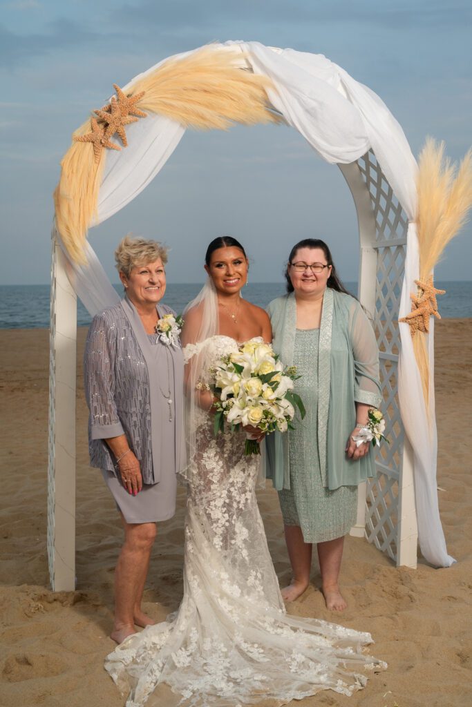 two women and a woman standing under an arch on the beach