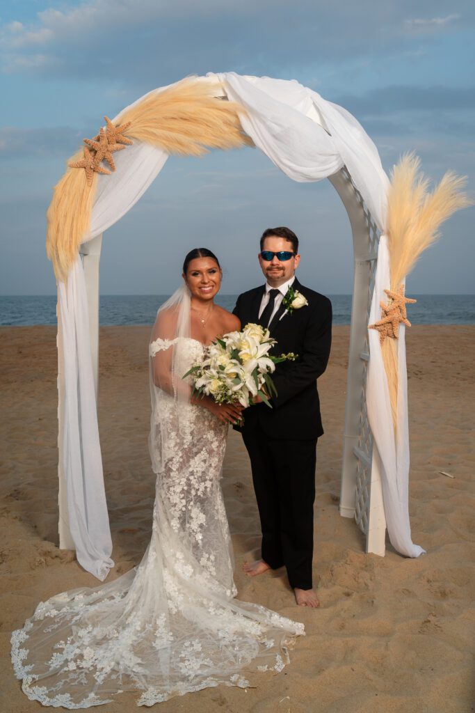 a bride and groom pose for a photo on the beach