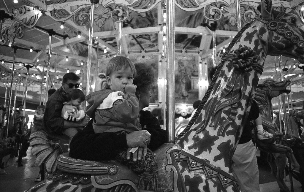 a little boy riding on the back of a merry go round