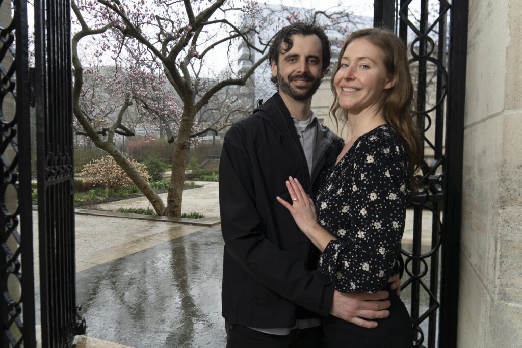 a man and woman standing next to each other in front of a gate