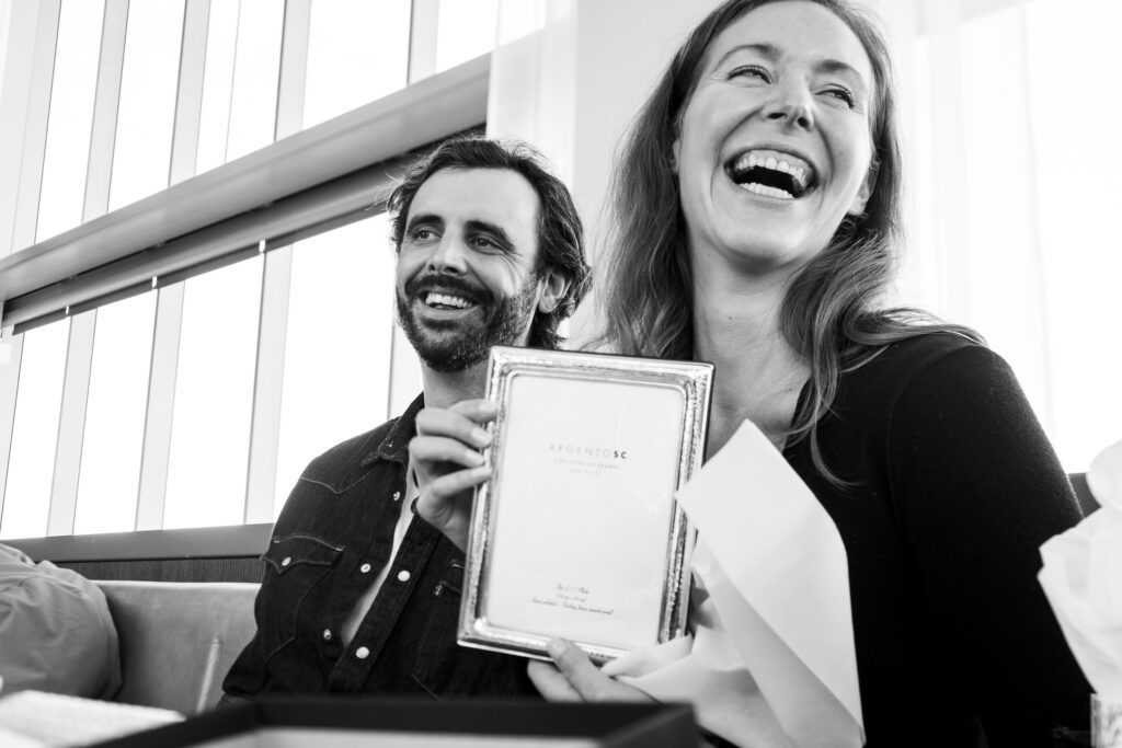 a man and woman smile as they hold an award