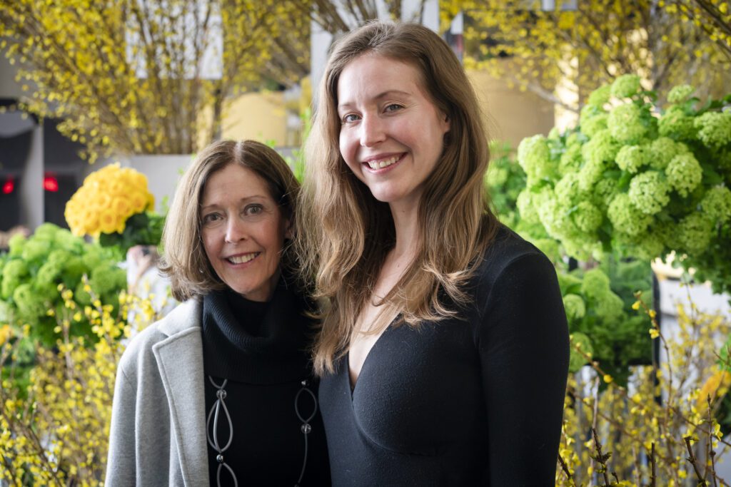 two women standing next to each other in front of flowers