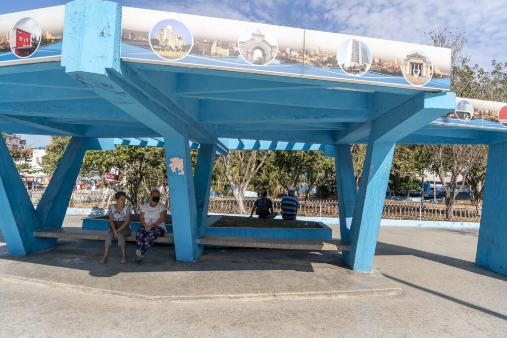 a couple of people sitting on a bench under a blue structure