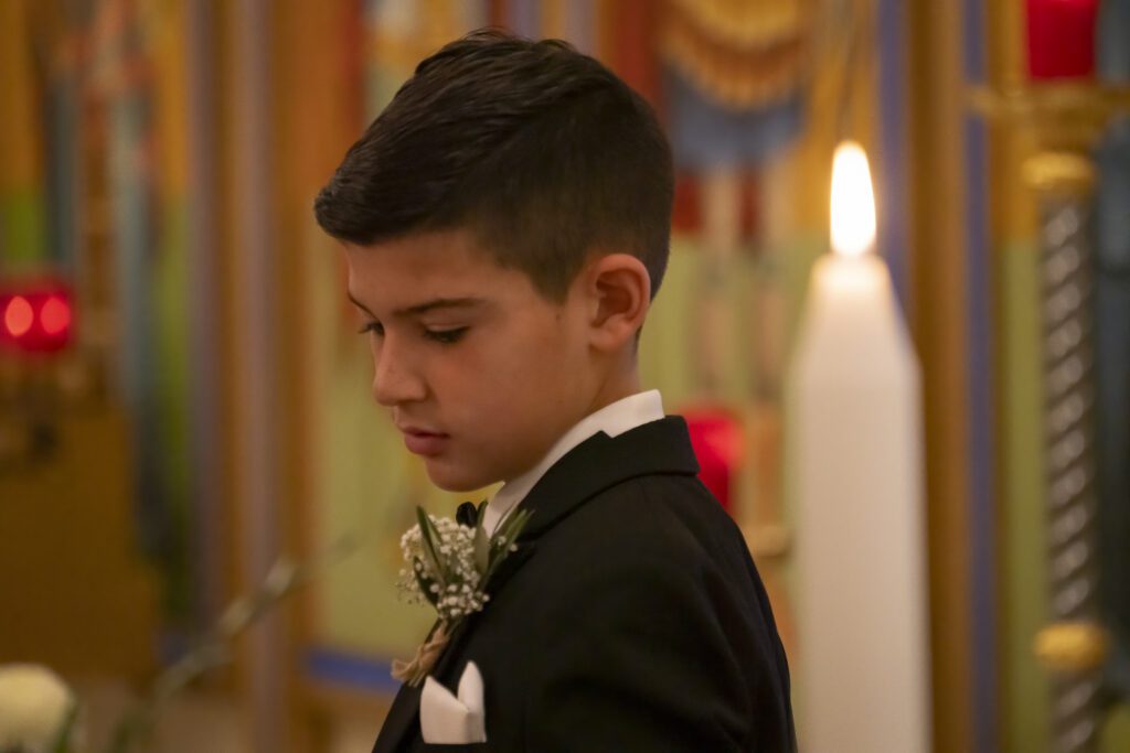 a young boy in a tuxedo standing in front of a candle