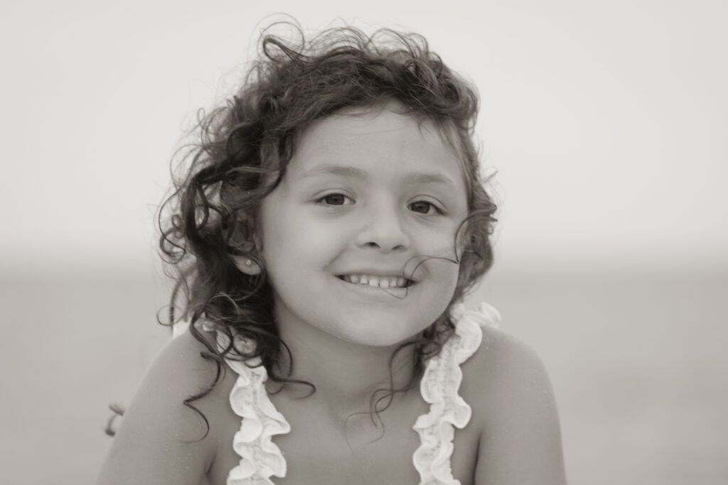 a little girl sitting on the beach with a smile on her face