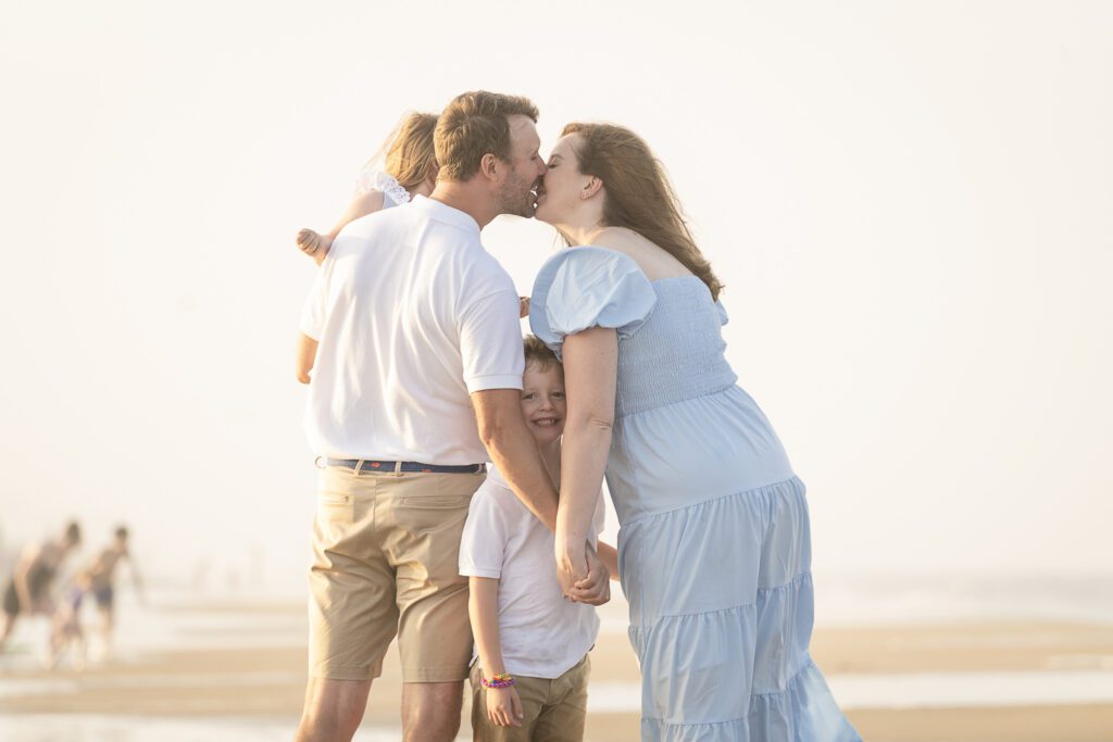a man and woman kissing a little boy on the beach