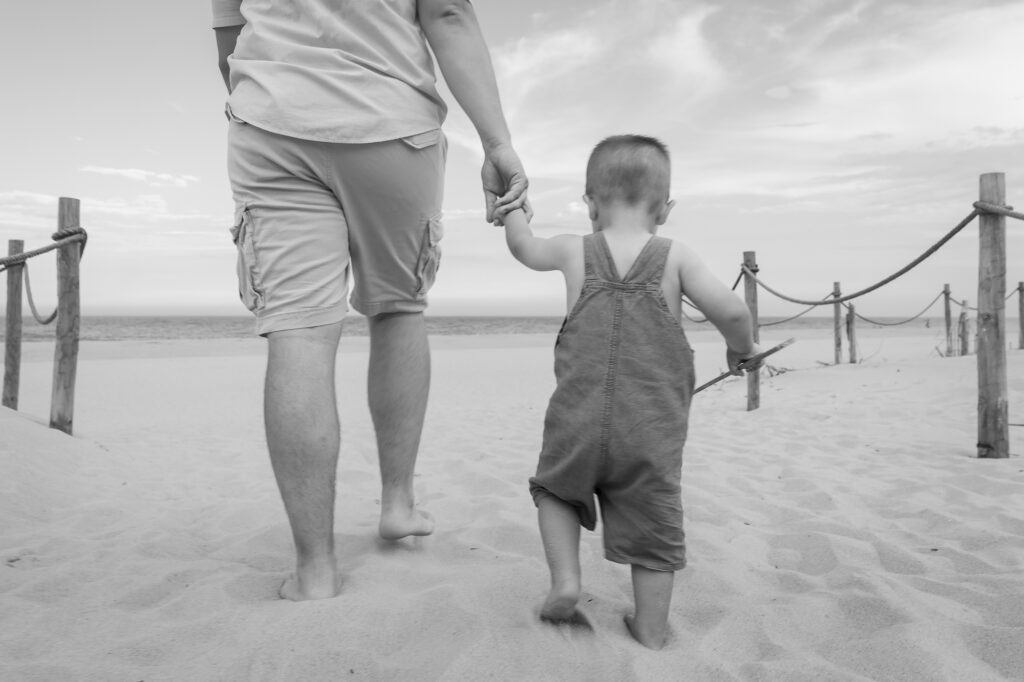a man holding the hand of a little boy on a beach