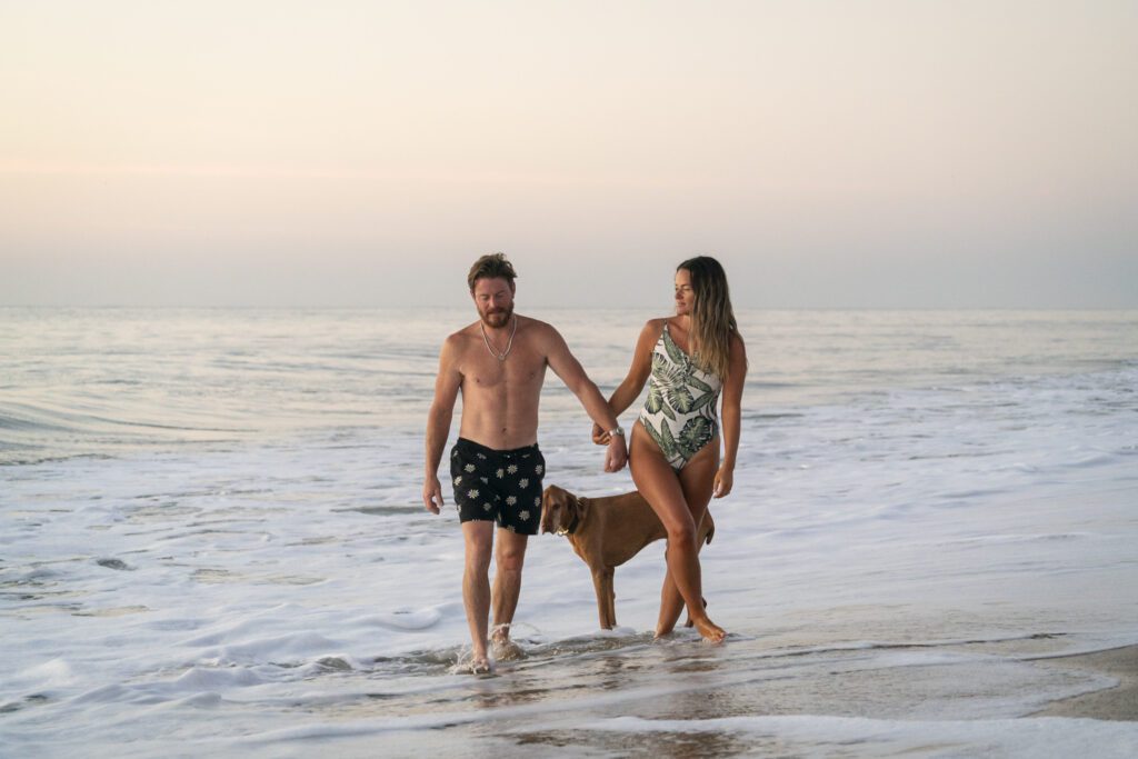 a man and a woman walking on the beach with a dog