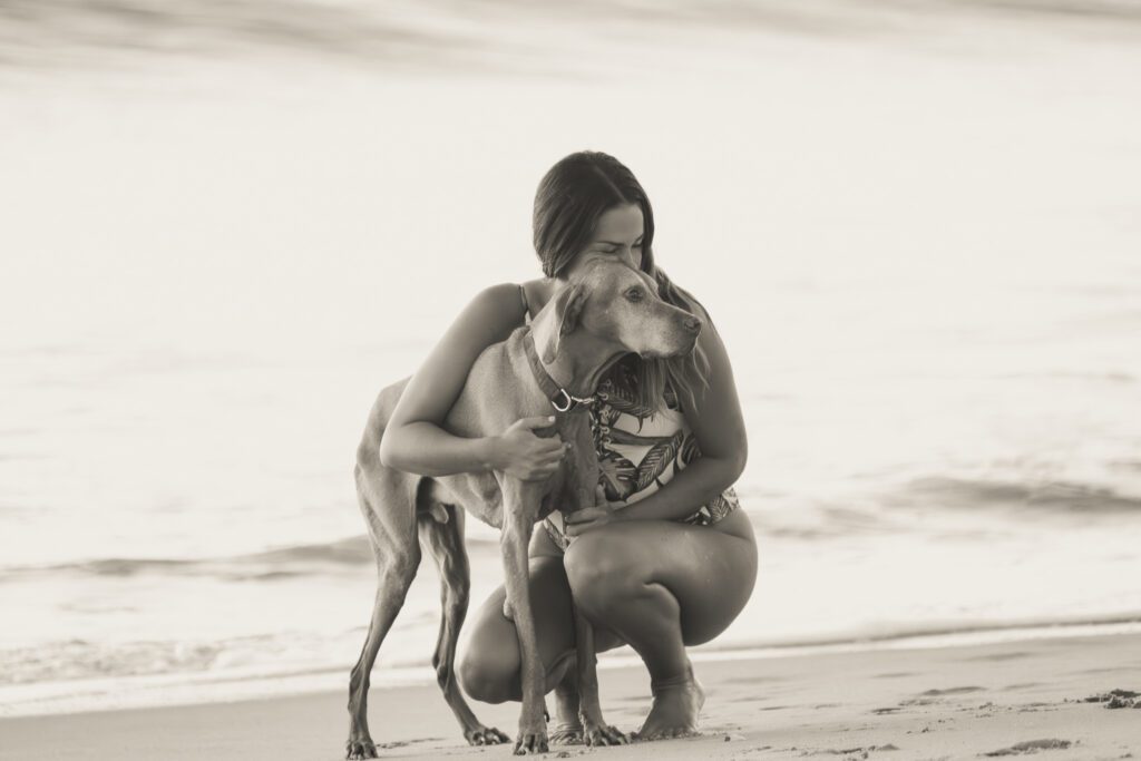 a woman kneeling down next to a dog on a beach