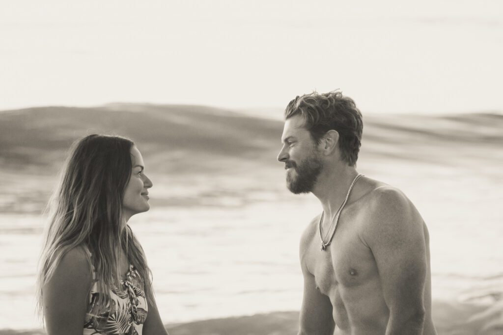 a man standing next to a woman on top of a beach