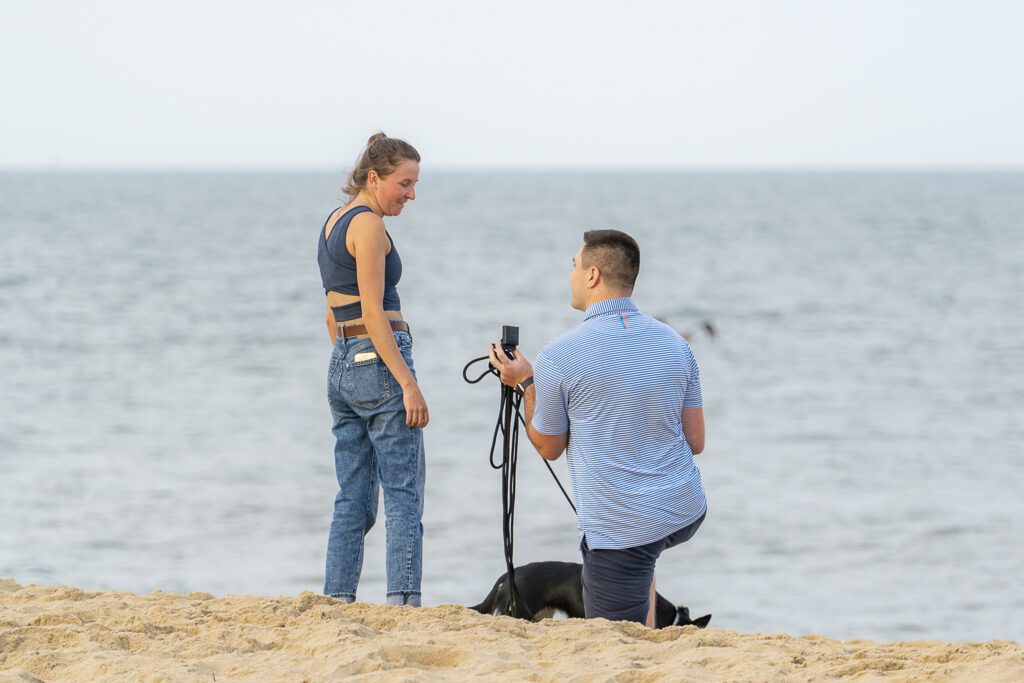 a woman taking a picture of a man and a dog on the beach